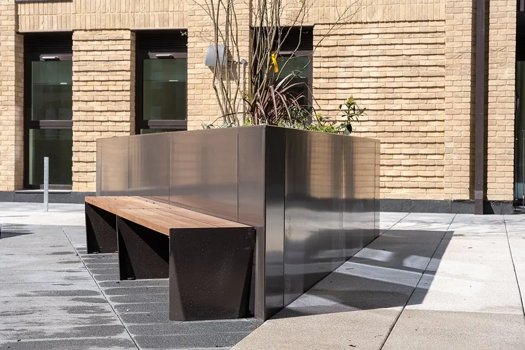 Timber seating beside a metal planter in a paved courtyard
